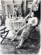 Assis, jambes étendues, table et bouquet - 1983