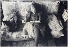 Assis pouf, robe noire, lit un papier - 1985