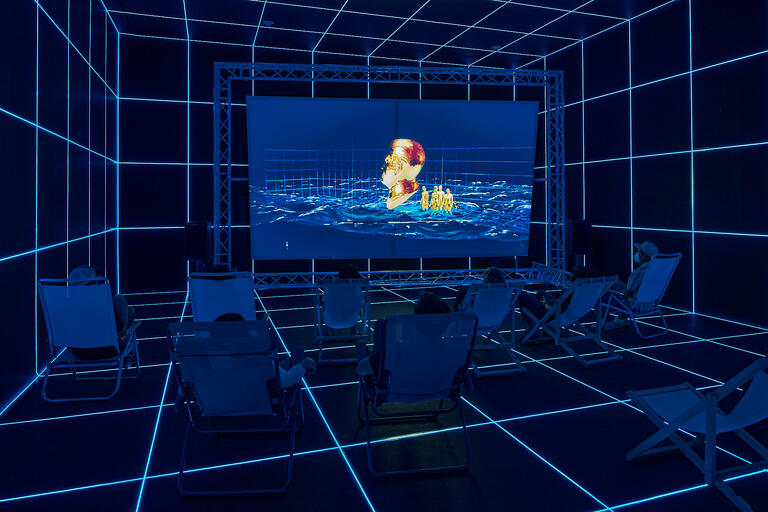 People seated in a dark room of a glowing blue grid, watching a surreal video.